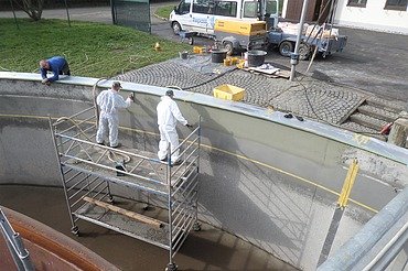 Klärbecken Foto von einem Klärbecken und zwei Männern auf einem Rollgerüst die Spachtelarbeiten ausführen