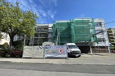 Sanierung von Balkonen Mehrfamilienhaus Foto von einem eingrüsteten Gebäude mit Fangnetz, Schuttrutsche und Sprinter