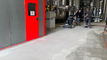 Foto von zwei Mitarbeitern die einen Raum entschichten und schleifen